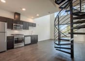 Thumbnail 22 of 41 - a kitchen with dark cabinets and stainless steel appliances and a spiral staircase leading up to a loft at THE ANGELINO, Sacramento, 95819