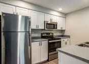 Thumbnail 9 of 63 - Kitchen with Stainless Appliances, Grey Countertops, White Cabinetry, and Wood-Style Flooring at BELLA SONOMA, Fife, WA