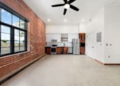 Thumbnail 18 of 81 - an empty living room with a brick wall and a kitchen with a ceiling fan