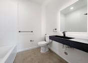 Thumbnail 23 of 81 - Pet-Friendly Apartments in Upper Land Park Sacramento CA - Market Club at The Mill - Plain Bathroom with Concrete Floor, White Walls, Toilet, Black Hardware and Sinktop Shower, and Tub