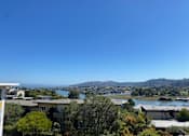 Thumbnail 1 of 19 - A view of a residential area with houses and trees in the foreground and a body of water and mountains in the distance.at Via Casitas, Greenbrae