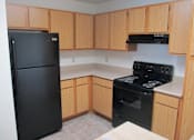 Thumbnail 2 of 28 - A black refrigerator and oven in a kitchen with wooden cabinets.