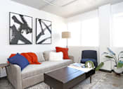 Thumbnail 8 of 20 - A living room with a grey couch, a coffee table, and two abstract black and white paintings on the wall at LOFT 205 Apartments, Reno, Nevada
