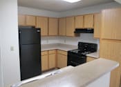 Thumbnail 1 of 28 - A black refrigerator and stove in a kitchen with wooden cabinets.