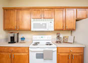 Thumbnail 4 of 34 - A kitchen with wooden cabinets and a white stove top oven. at Fairview Village Homes, Fairview