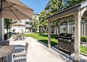Thumbnail 5 of 20 - A patio with a grill and chairs under an umbrella.