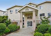 Thumbnail 1 of 26 - A beige building with a front entrance and bushes at Vintage at Burien,Burien,98168