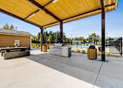 Thumbnail 10 of 18 - A central stainless steel grilling station, two wood-slat trash bins, and a picnic dining table with a small floral arrangement at View by Vintage Apartments, Washington