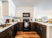 Thumbnail 16 of 18 - A modern kitchen with dark wood cabinets and a white countertop at View by Vintage Apartments, Bonney Lake, WA