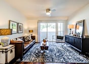 Thumbnail 13 of 18 - A living room with a brown leather couch, a black and white lamp, a brown coffee table, a black rug, a black dresser, a black chair, a black mirror, a white ceiling fan, a white wall at View by Vintag