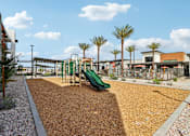 Thumbnail 13 of 32 - A playground with a green slide and brown mulch at Ironwood Ranch Apartments,Maricopa,AZ,85138