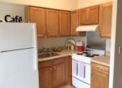 Thumbnail 8 of 10 - A kitchen with wooden cabinets and a white refrigerator at Tabco Towers Apartments, Maryland, 21286