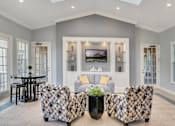 Thumbnail 5 of 24 - A living room with a patterned chair and a television on the wall at The Villages on Millenia Apartments, Orlando 32839