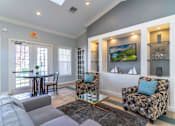 Thumbnail 6 of 24 - A living room with a grey couch, a patterned armchair, and a television mounted on the wall at The Villages on Millenia Apartments, Florida