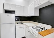 Thumbnail 12 of 17 - A white refrigerator is in a kitchen with white cabinets and a white stove.