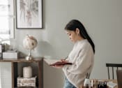 Thumbnail 14 of 17 - A woman in a white sweater is writing in a notebook.