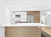 Thumbnail 18 of 56 - A modern kitchen with a white countertop and wooden cabinets.