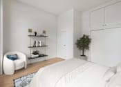 Thumbnail 4 of 9 - A white bedroom with a bed, chair, and shelves.