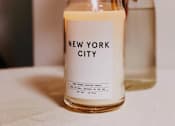 Thumbnail 9 of 9 - A New York City scented candle is lit and placed on a table.