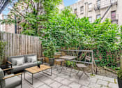 Thumbnail 1 of 18 - A patio with a table and chairs surrounded by green plants.