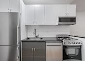 Thumbnail 14 of 18 - A modern kitchen with a stainless steel refrigerator, black countertop, and white cabinets.