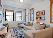 Thumbnail 12 of 19 - A living room with a couch, a rug, and a bookshelf.