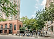 Thumbnail 16 of 18 - A red brick building with arched windows sits between a tree and a tall building.