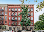 Thumbnail 1 of 18 - A red brick building with black fire escapes on the side.