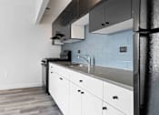 Thumbnail 12 of 22 - A kitchen with white cabinets and a black refrigerator.