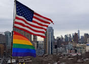 Thumbnail 7 of 9 - A rainbow flag is displayed next to an American flag in a city.