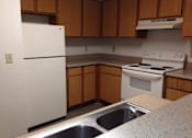 Thumbnail 25 of 28 - A white refrigerator is in a kitchen with wooden cabinets.