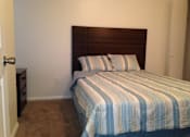Thumbnail 26 of 28 - A bed with a blue and white striped comforter sits in a room with a brown headboard.