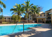 Thumbnail 4 of 20 - Portofino Apartments resort style pool and lounge chairs with palm tree in lush greenery at Portofino, Florida