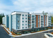 Thumbnail 3 of 22 - Complex with Parking Lot Access, Tall Trees, and Blue Skies at QUINN BY VINTAGE, Shoreline, WA