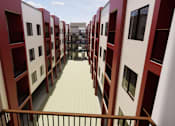 Thumbnail 4 of 7 - A long hallway with red and white buildings on either side at Vintage at Lockwood Apartments, Oxnard, California