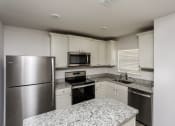 Thumbnail 9 of 33 - 4 Bedroom Single Family Homes for Rent in Newark TX - Chisholm Springs - Modern Kitchen with Granite Countertops, Stainless Steel Appliances, White Cabinetry, and Wood-Style Flooring