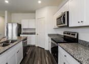 Thumbnail 6 of 32 - Four BR Homes in Haslet TX - Willow Springs - Modern Ktichen with Stainless Steel Appliances, Granite Countertops, White Cabinetry, and Wood-Style Flooring