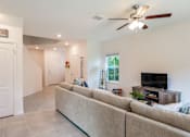 Thumbnail 4 of 56 - A cozy living room with a large sectional sofa, a ceiling fan, a TV on a wooden stand, and a staircase leading to the upper floor.