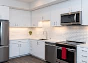 Thumbnail 1 of 20 - Oakland, CA, Apartments Near Whole Foods - Telegraph Arts - Kitchen With Wood-Style Flooring, White Cabinets, Granite Countertops, Subway Tile Backsplash, and Stainless Steel Appliances.
