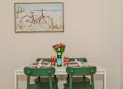 Thumbnail 26 of 56 - A dining table with two green chairs and a painting of a bicycle on the wall.