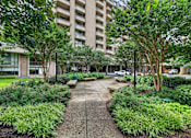 Thumbnail 63 of 66 - A concrete walkway leads through a landscaped area with a large building in the background.