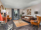 Thumbnail 21 of 34 - A living room with a brown sofa, a black and white patterned chair, and a wooden coffee table.