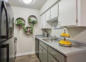 Thumbnail 6 of 46 - Dog-Friendly Apartments in Mesa, AZ - Mesa Station Apartments - Kitchen With White Cabinets, Gray Countertops, Stainless Steel Appliances, Single Basin Sink, And Decorative Wall Greenery.