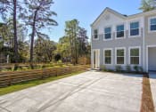 Thumbnail 8 of 25 - Pet-Friendly Homes for Rent in North Charleston, SC - Sumner Village - Front Exterior of Apartment Home with Driveway, Wooden Fence, and View of Trees and Bushes.