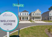 Thumbnail 23 of 25 - Houses for Rent in North Charleston, SC - Sumner Village - Street View of Apartment Homes with Driveways, Sidewalk, Manicured Lawns, and Property Signage.
