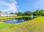 Thumbnail 29 of 62 - Myrtle Beach, SC Homes for Rent - The Palmer at Carolina Forest - Pond with Fountain, Surrounded by Maintained Grass Lawn, Trees, and Homes