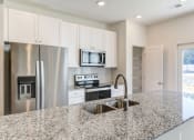 Thumbnail 5 of 45 - North Charleston, SC Townhomes Near The Citadel - Highland Townhomes - Kitchen With Stainless Steel Appliances, White Cabinets, White Tile Backsplash, White Walls, and Granite Countertops