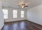 Thumbnail 19 of 45 - Townhouses for Rent in North Charleston, SC - Highland Townhomes - Empty Living Room with Hardwood Floor, Multiple Windows, White Walls, and Ceiling Fan.