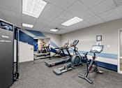 Thumbnail 32 of 47 - A gym with a Nautilus machine, a treadmill, a stationary bike, and a weight bench.