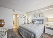 Thumbnail 12 of 46 - Two-Bedroom Apartments in Mesa, AZ - Mesa Station Apartments - Bedroom With Gray Bedding, Upholstered Headboard, Nightstands, Table Lamps, Wall Decor, Carpeted Flooring, And Laundry Room Access.